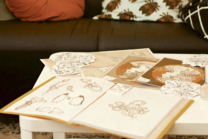 Cadernos de flash abertos sobre a mesa do salão, com desenhos a traço e gravuras em tons de ocre