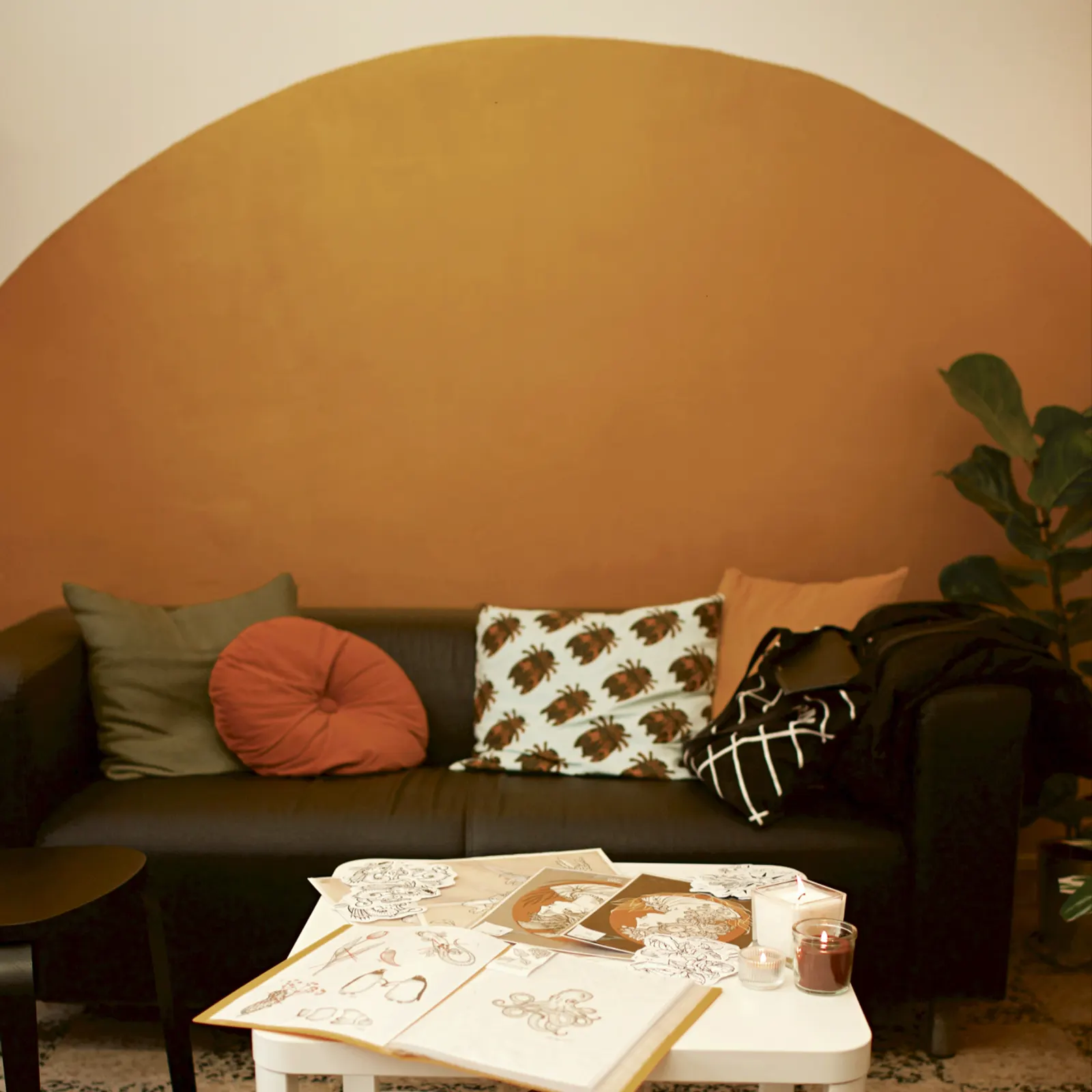 O salão da Aurora: meio sol ocre pintado na parede branca, sofá de couro preto, e na mesa os cadernos de flash abertos à luz das velas